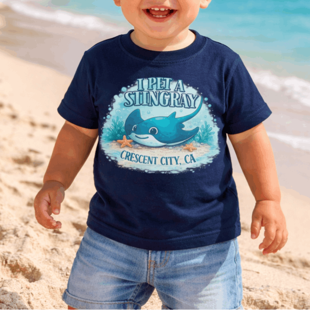Child wearing a navy blue t-shirt with a graphic design of a stingray underwater and text I Pet a Stingray Crescent City, CA.