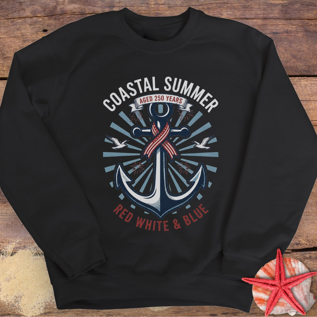 Black sweatshirt with 'Coastal Summer' design featuring an anchor and American flag on a wooden surface.