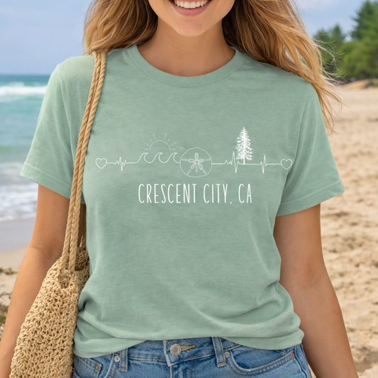 Person wearing a sage green t-shirt with 'Crescent City, California' Varsity text with Est. 1854.