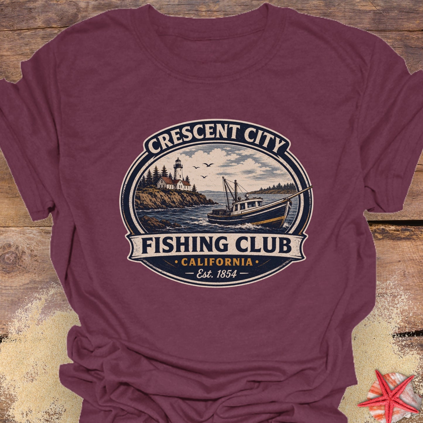 A maroon short-sleeve crewneck t-shirt featuring a circular vintage-style graphic that reads 'Crescent City Fishing Club California Est. 1854' with an illustration of a fishing boat on the water.