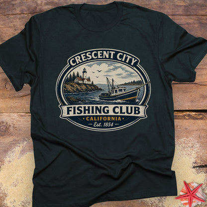 A dark charcoal gray t-shirt with a vintage-style circular graphic reading 'Crescent City Fishing Club California Est. 1854', laid flat on a rustic wooden surface with a small red starfish prop in the corner.