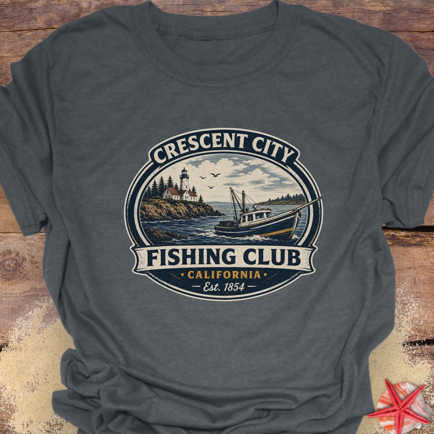 A dark gray crewneck t-shirt featuring a vintage-style circular graphic that reads 'Crescent City Fishing Club California Est. 1854' with an illustration of a lighthouse, boat, and ocean.