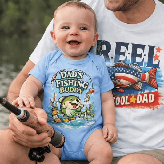 Man holding a baby wearing a 'Dad's Fishing Buddy' onesie by a body of water.