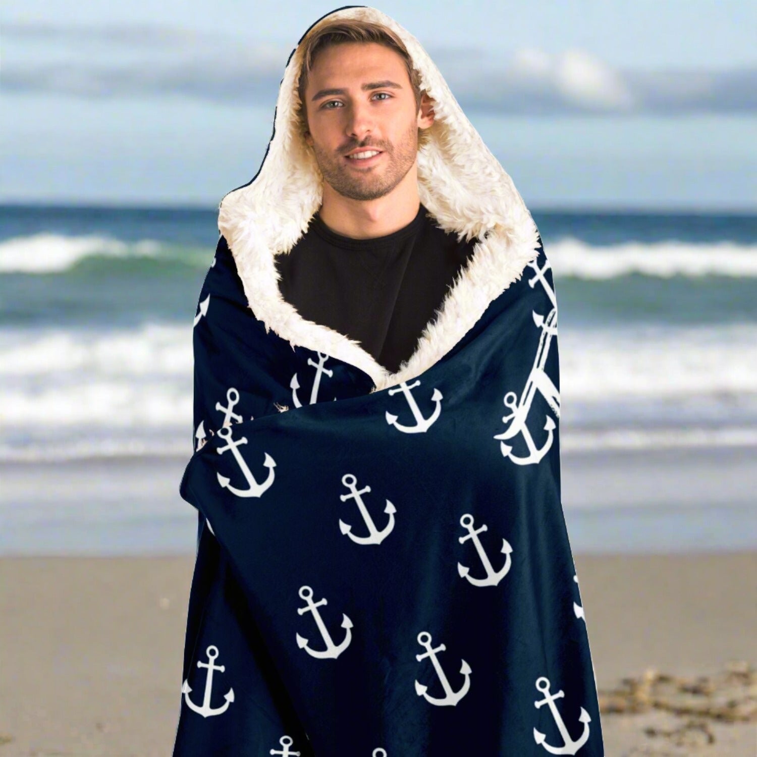 Person on the beach wrapped in a dark blue hooded blanket with white anchors and white writing that says The Ocean is my Anchor