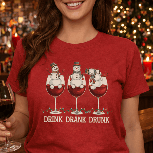 Person wearing a red t-shirt with a fun Christmas-themed design of 3 wine glasses with snowmen inside and text Drink Dank Drunk.