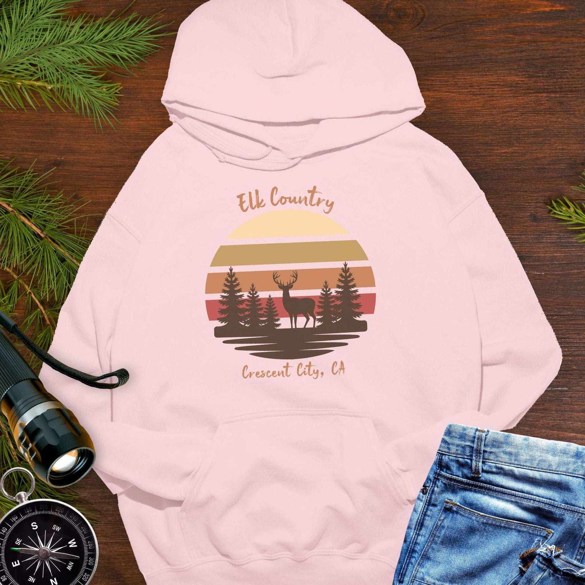 Pink hoodie with 'Elk Country' with retro sunset and silhouette of trees and elk design with Crescent City, CA underneath.