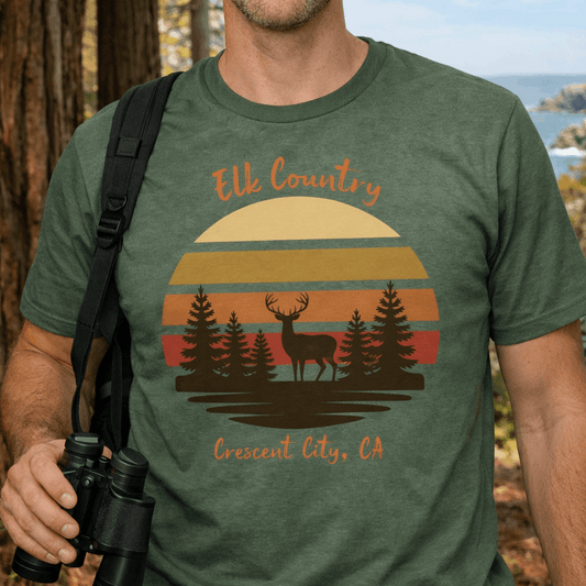 Person wearing a military green t-shirt with 'Elk Country' retro sunset with an elk and redwoods design with text Elk Country Crescent City, CA.
