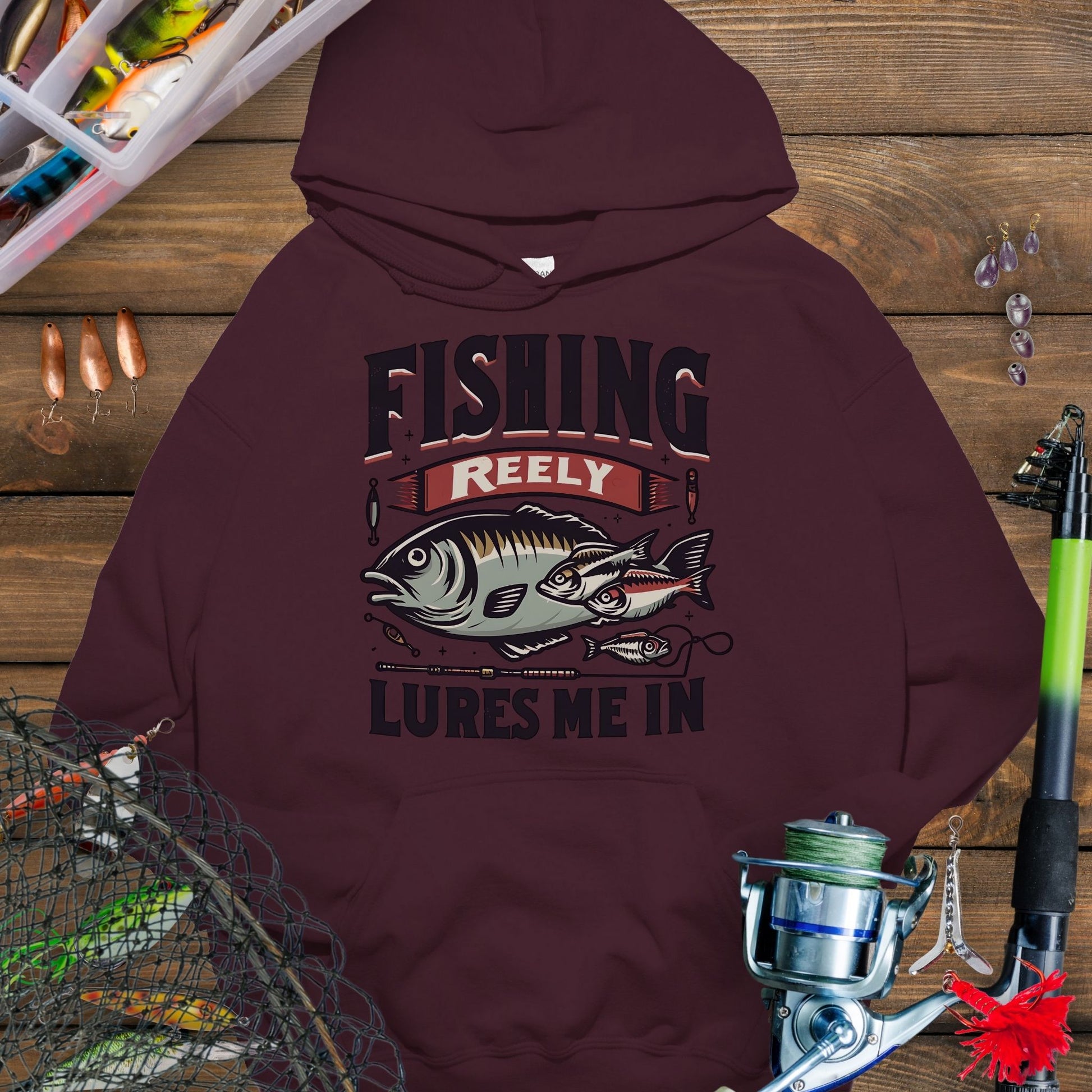 Maroon  fishing hoodie with fish and tackle graphics and the phrase “Fishing Reely Lures Me In”.