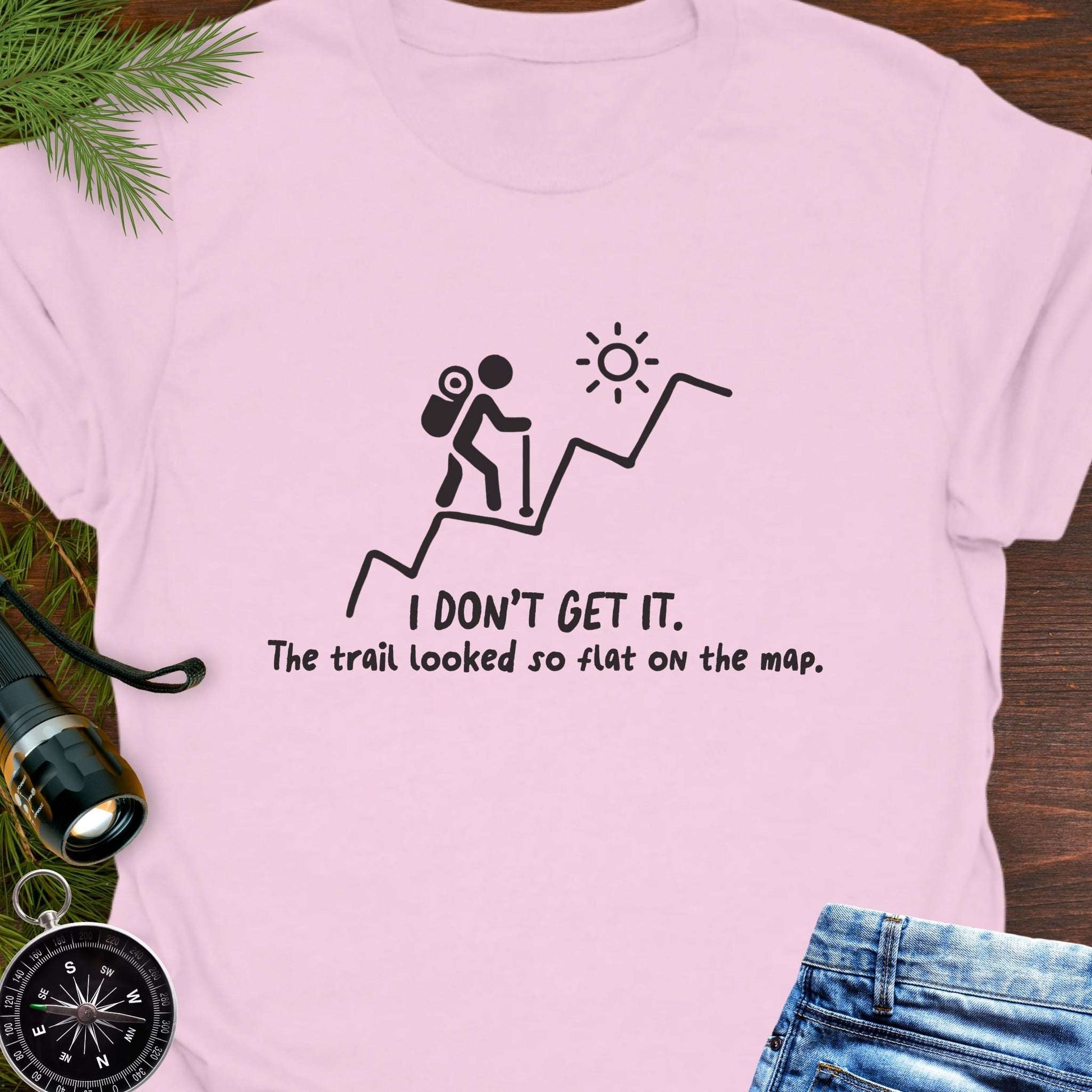 Pink hiking t-shirt flat lay with black graphic of a backpacker climbing a steep trail and text: “I DON’T GET IT. The trail looked so flat on the map.”