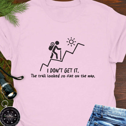 Pink hiking t-shirt flat lay with black graphic of a backpacker climbing a steep trail and text: “I DON’T GET IT. The trail looked so flat on the map.”