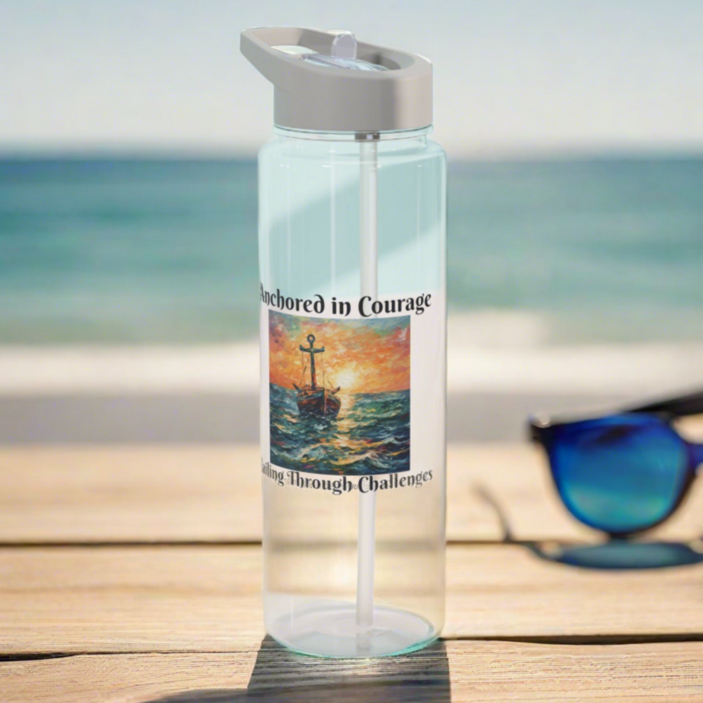 Clear Water Bottle with gray lid and straw with a picture of an old ship that says Anchored in Courage and Sailing through Challenges around it sitting on a beach