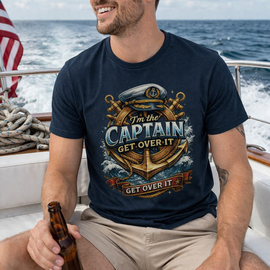Man wearing a navy blue unisex t-shirt with nautical anchor and ship wheel graphic and text “I’m the Captain Get Over It”.