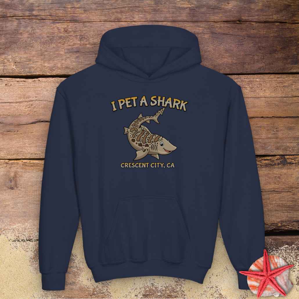 A navy blue pullover hoodie with a graphic print of a shark and the text 'I PET A SHARK' and 'CRESCENT CITY, CA'.