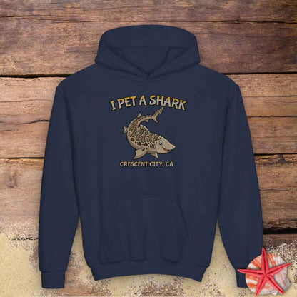 A navy blue pullover hoodie with a graphic print of a shark and the text 'I PET A SHARK' and 'CRESCENT CITY, CA'.