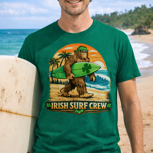 Person wearing a green t-shirt with Bigfoot carrying a shamrock-decorated surfboard at the beach, with text “Irish Surf Crew”.