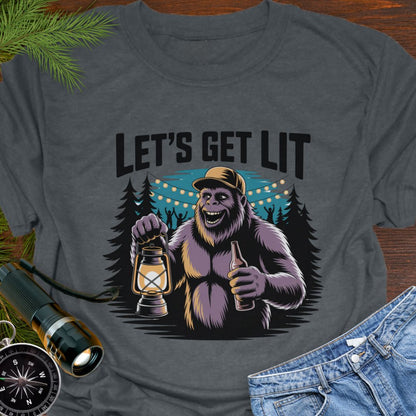 Dark Heather "Let's Get Lit" Sasquatch T-Shirt  featuring a sasquatch wearing a baseball hat holding a camping lantern and a beer in a party scene in the woods.