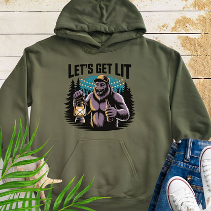 Military Green funny Sasquatch camping unisex hoodie with relaxed outdoor party vibe that says Let's Get Lit featuring a sasquatch wearing a ball cap holding a camping lantern and a bottle of beer with the forest in a forest camp scene.