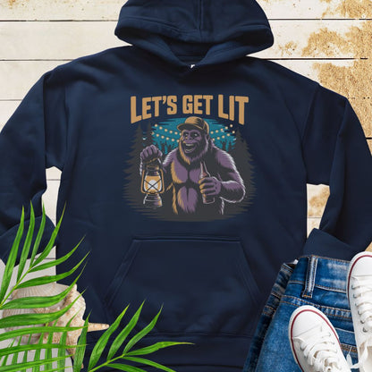 Navy funny Sasquatch camping unisex hoodie with relaxed outdoor party vibe that says Let's Get Lit featuring a sasquatch wearing a ball cap holding a camping lantern and a bottle of beer with the forest in a forest camp scene.