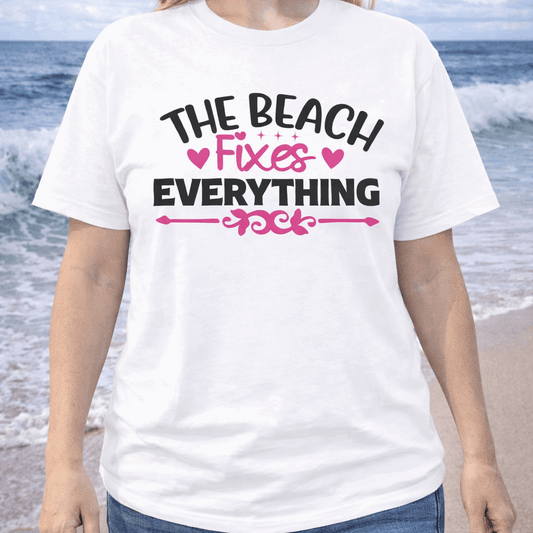 Person wearing a white t-shirt with 'The Beach Fixes Everything' text on a beach.