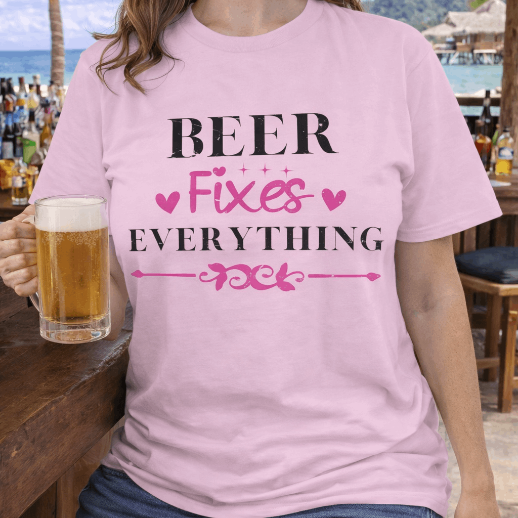 Person wearing a pink t-shirt with 'Beer Fixes Everything' text, holding a beer at a beachside bar.