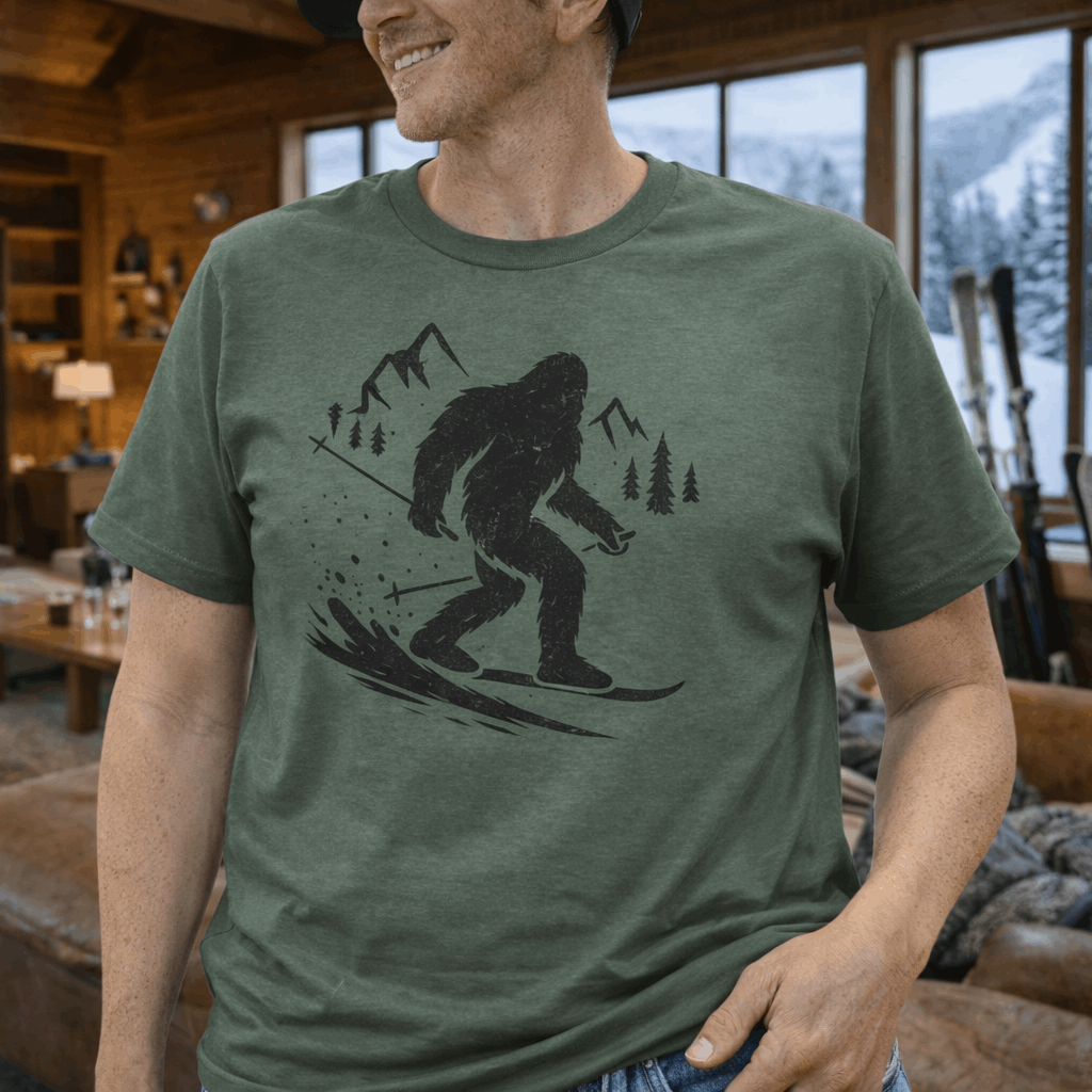A military green t-shirt with a bigfoot skiing down a mountain black graphic.