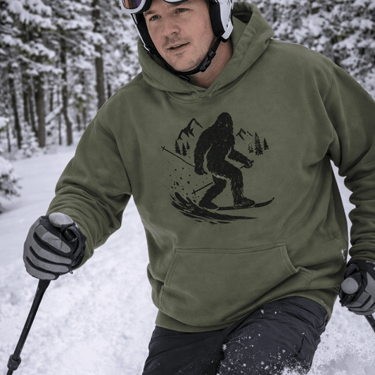 Person skiing in a snowy forest wearing a green hoodie with a Sasquatch graphic.
