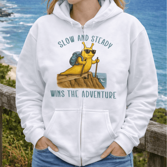 Woman wearing a white hoodie with a hiking banana slug and text Slow and Steady Wins the Adventure.