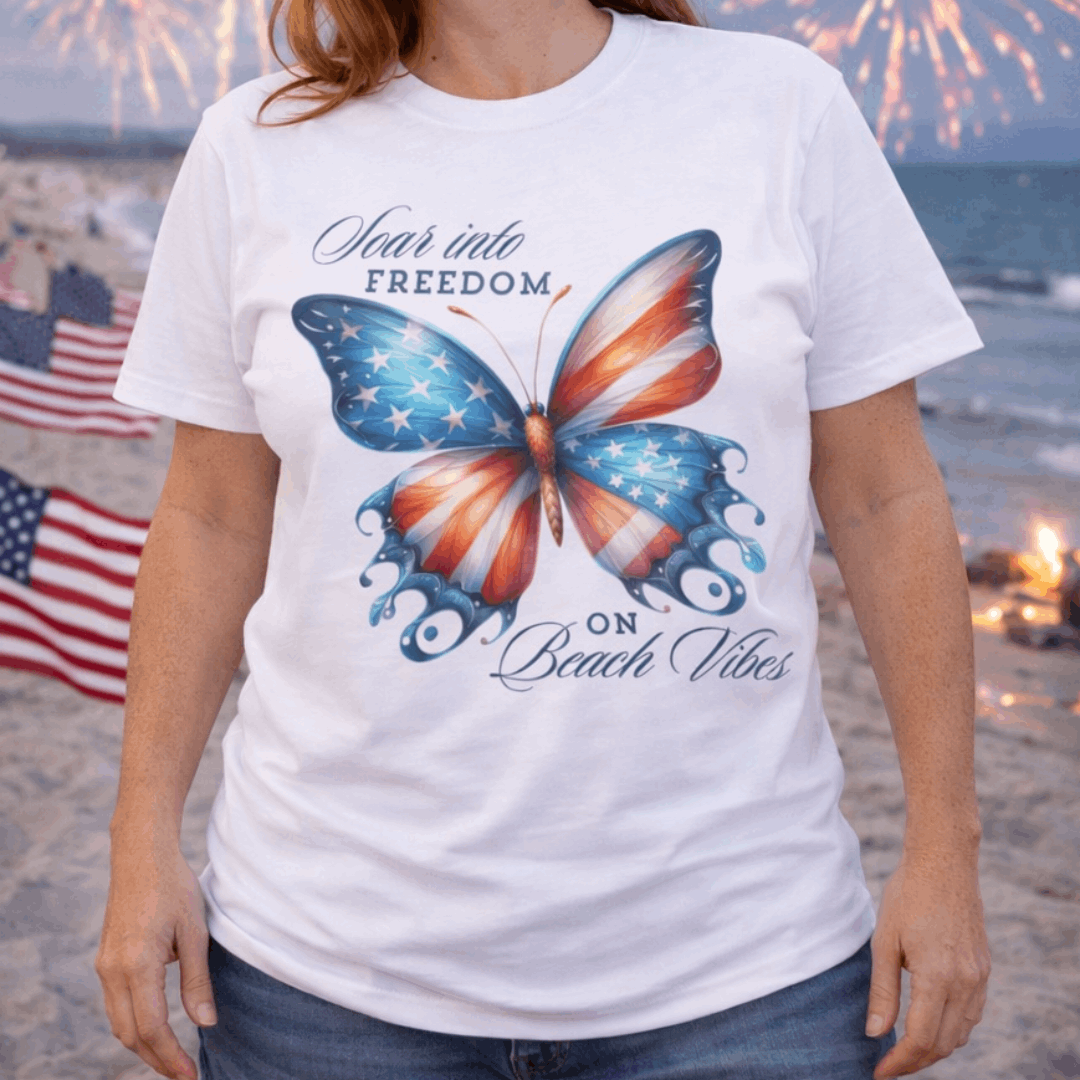 Person wearing a white t-shirt with an American flag butterfly graphic and text 'Soar into Freedom on Beach Vibes'.