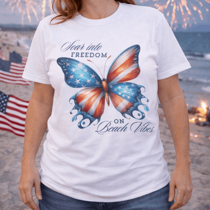 Person wearing a white t-shirt with an American flag butterfly graphic and text 'Soar into Freedom on Beach Vibes'.