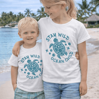 Two children wearing 'Stay Wild Ocean Girl' t-shirts on a beach.