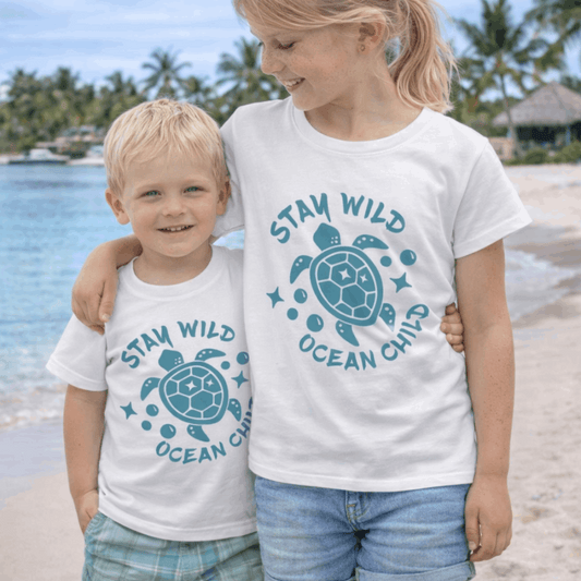 Two children wearing 'Stay Wild Ocean Girl' t-shirts on a beach.