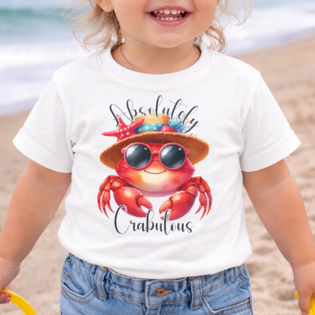 Child on a beach wearing a white t-shirt with a colorful crab design and text Absolutely Crabulous.