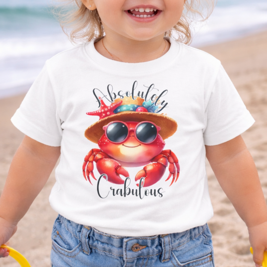 Child on a beach wearing a white t-shirt with a colorful crab design and text Absolutely Crabulous.