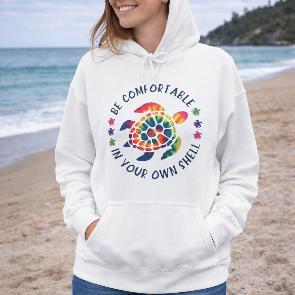 Person wearing a white hoodie with a colorful sea turtle design and text be comfortable in your own shell.