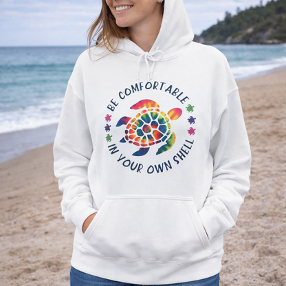 Person wearing a white hoodie with a colorful sea turtle design and text be comfortable in your own shell.