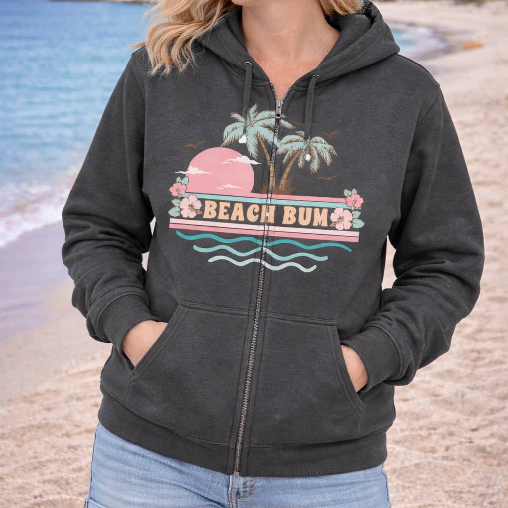 Woman wearing a 'Beach Bum' hoodie on a beach with palm trees and ocean in the background.