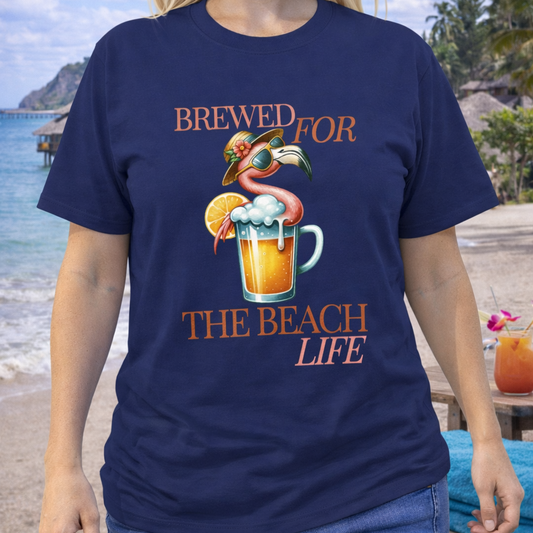 Person wearing a navy blue t-shirt with a flamingo and beer graphic with text brewed for the beach life. 