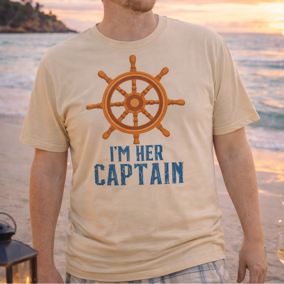 Man wearing a t-shirt with a ship's wheel and 'I'm Her Captain' text on a beach at sunset.