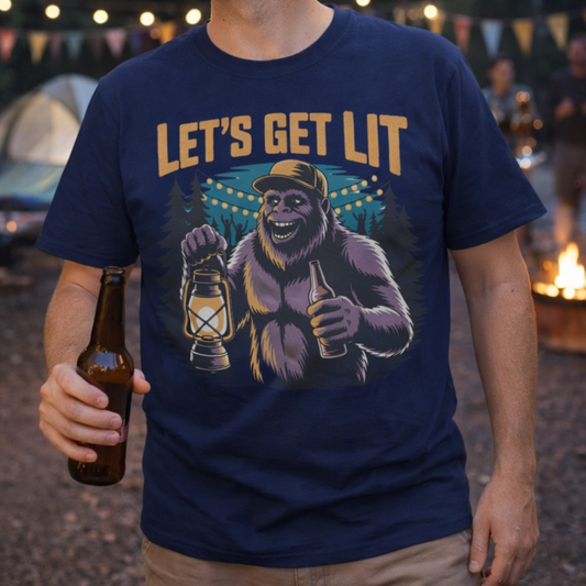 Man wearing a navy blue t-shirt with a sasquatch graphic and 'Let's Get Lit' text, holding a beer bottle at a campsite.