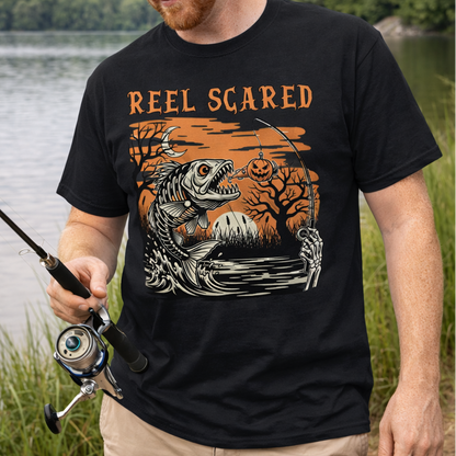 Man fishing by a lake wearing a black t-shirt with 'Reel Scared' graphic design.