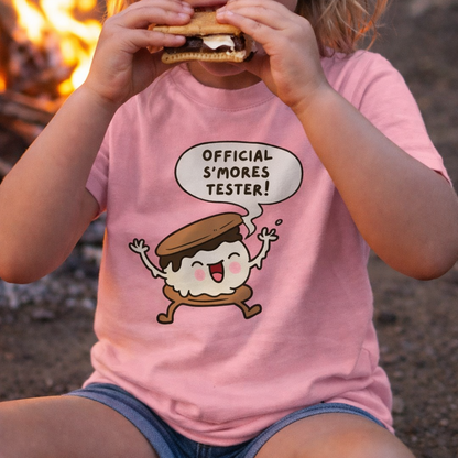 Child eating s'mores with a pink toddler t-shirt featuring a cartoon s'more character and text Official S'mores Tester.