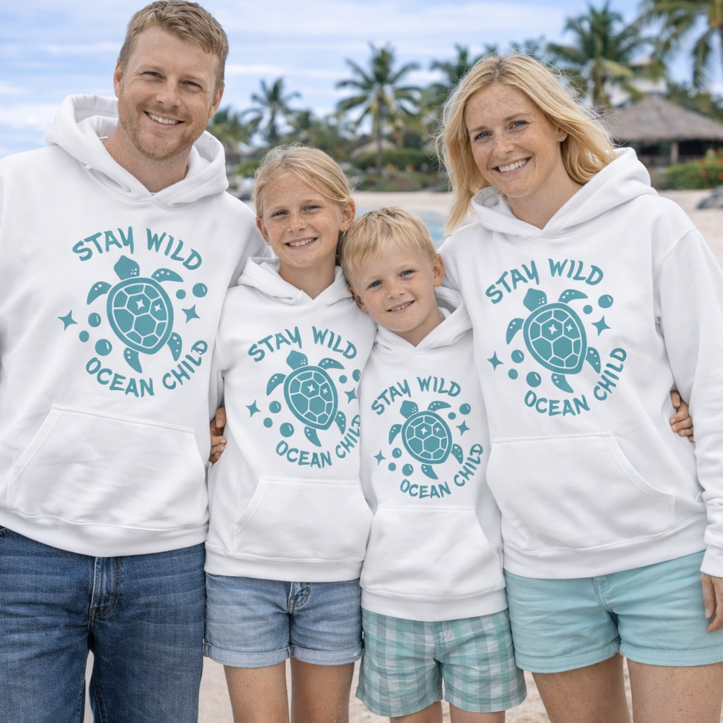 Family wearing a white hoodie with a sea turtle design and 'Stay Wild Ocean Child' text on a beach.