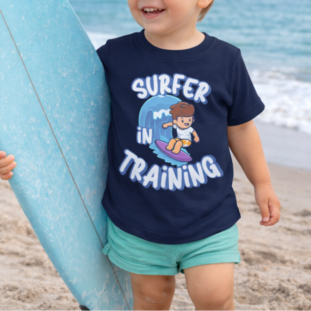 Child wearing a 'Surfer in Training' shirt on a beach