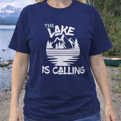 Person wearing a navy blue t-shirt with 'The Lake is Calling' design by a lakeside.