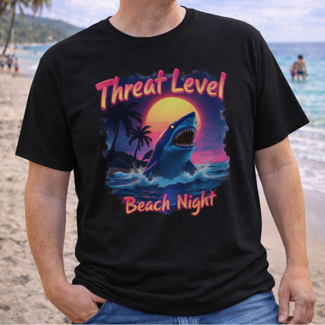 Person wearing a black t-shirt with a colorful graphic and text 'Threat Level Beach Night' on a beach.