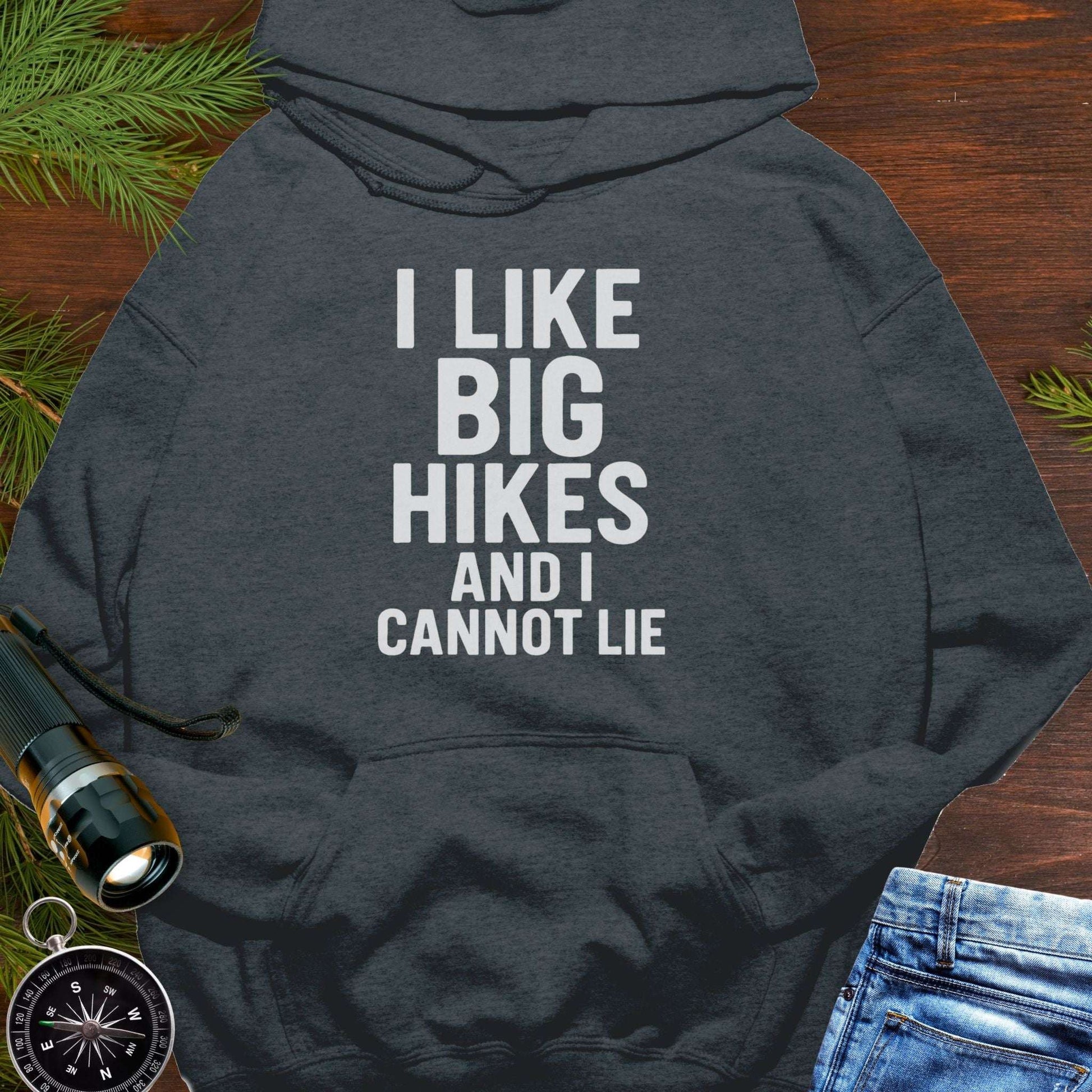 Dark gray hoodie with 'I LIKE BIG HIKES AND I CANNOT LIE' text on a wooden surface with hiking accessories.