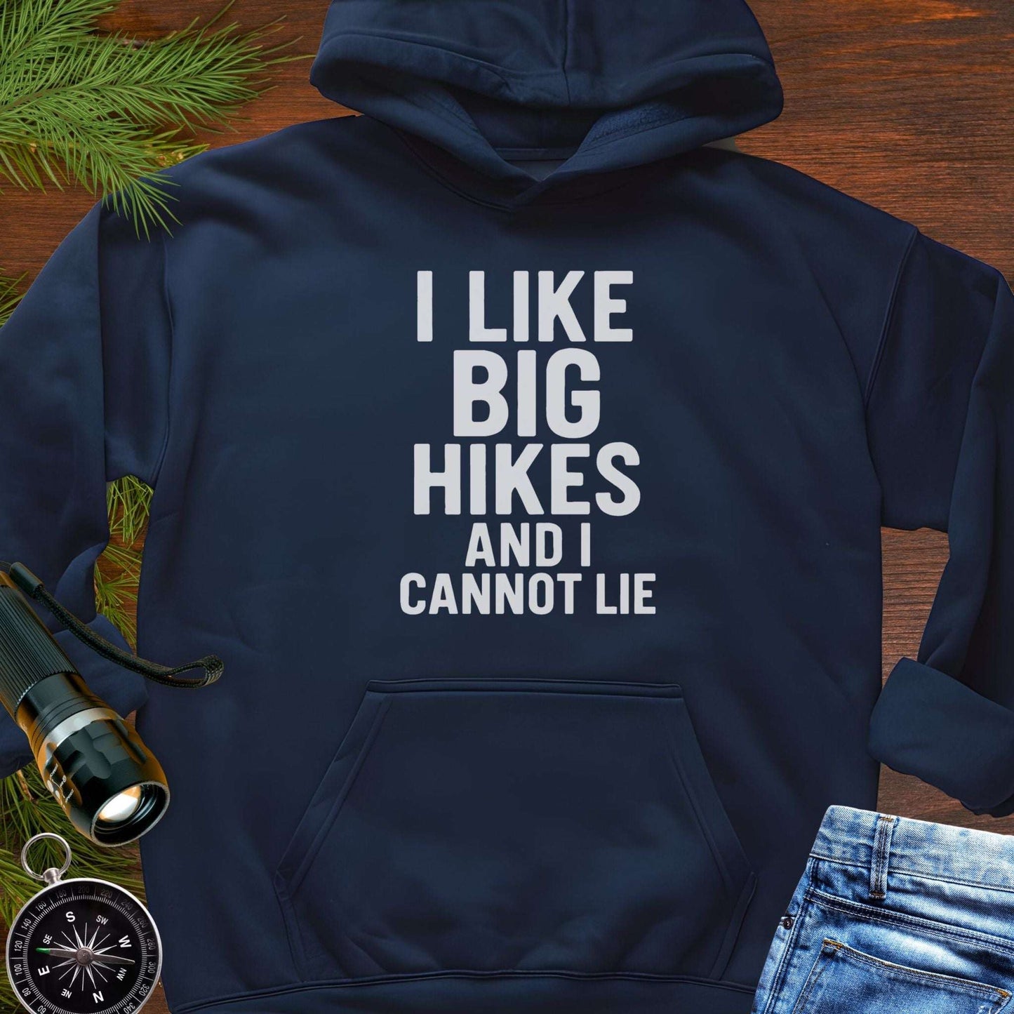 Navy blue hoodie with 'I LIKE BIG HIKES AND I CANNOT LIE' text on a wooden surface with hiking gear.