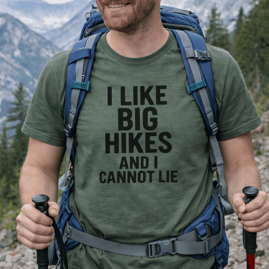 Man hiking with a green t-shirt that says 'I LIKE BIG HIKES AND I CANNOT LIE' in a mountainous area.