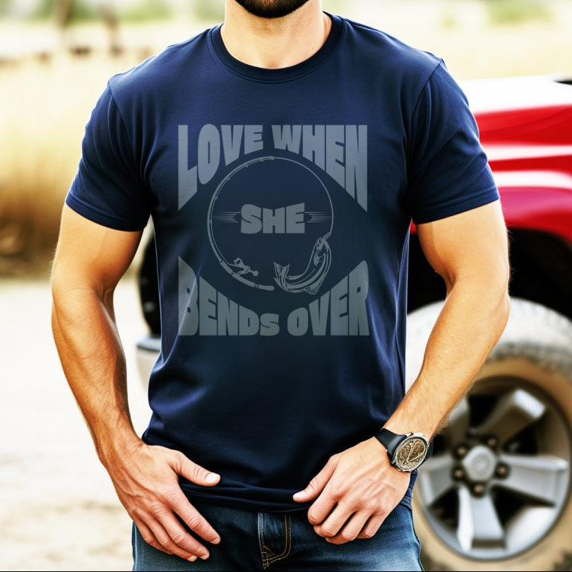Man wearing navy blue t-shirt with a fishing pole bending over and the phrase “Love When She Bends Over” – humorous fishing design for anglers.