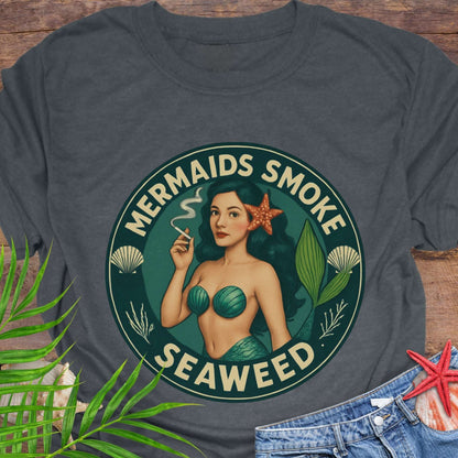 Gray t-shirt with a mermaid graphic and text 'Mermaids Smoke Seaweed' on a wooden surface.